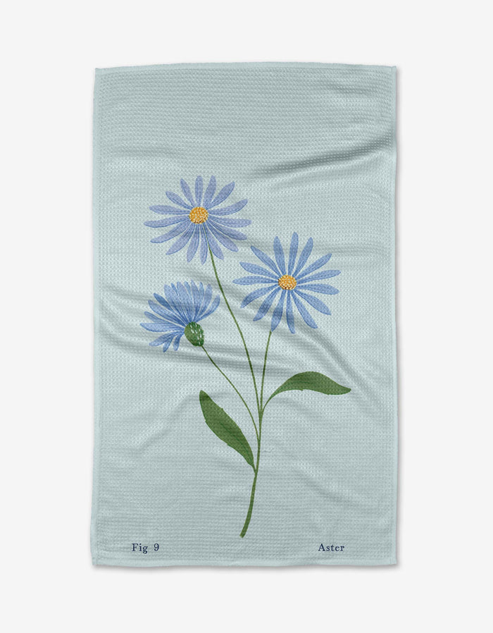 The September Aster Geoweave™ Tea Towel by Linda Fox features a pale blue design with a three-stemmed aster flower, green leaves, and purple petals. Made from recycled materials and printed with “Fig 9” and “Aster” at the bottom.