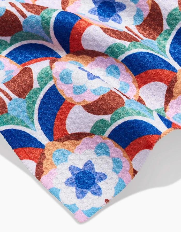 A close-up of the Claire Iglesias Seventies Retro Flowers bar towel shows its bold retro floral Geoweave fabric in blue, red, green, and brown on white. Slight folds highlight its soft texture and eco-friendly recycled materials.