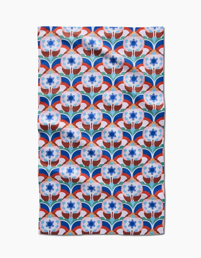 The Seventies Retro Flowers tea towel by Claire Iglesias features a blue and white floral pattern with red curved lines in a geometric retro style, made from recycled materials. Ultra-absorbent, slightly wrinkled fabric on a white background.