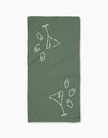 The Shaken Not Stirred bar towel by Rosa Kichline is green, rectangular, and features two white outlined martini glasses with scattered olives in a minimalist style. Made from ultra-absorbent recycled materials for eco-friendly use.