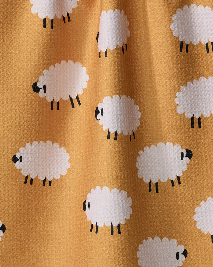 The "Sheep" tea towel by Jennifer Bouron features a yellow geometric design with a textured fabric and a playful pattern of cartoon white sheep with black faces and legs, scattered in different directions.