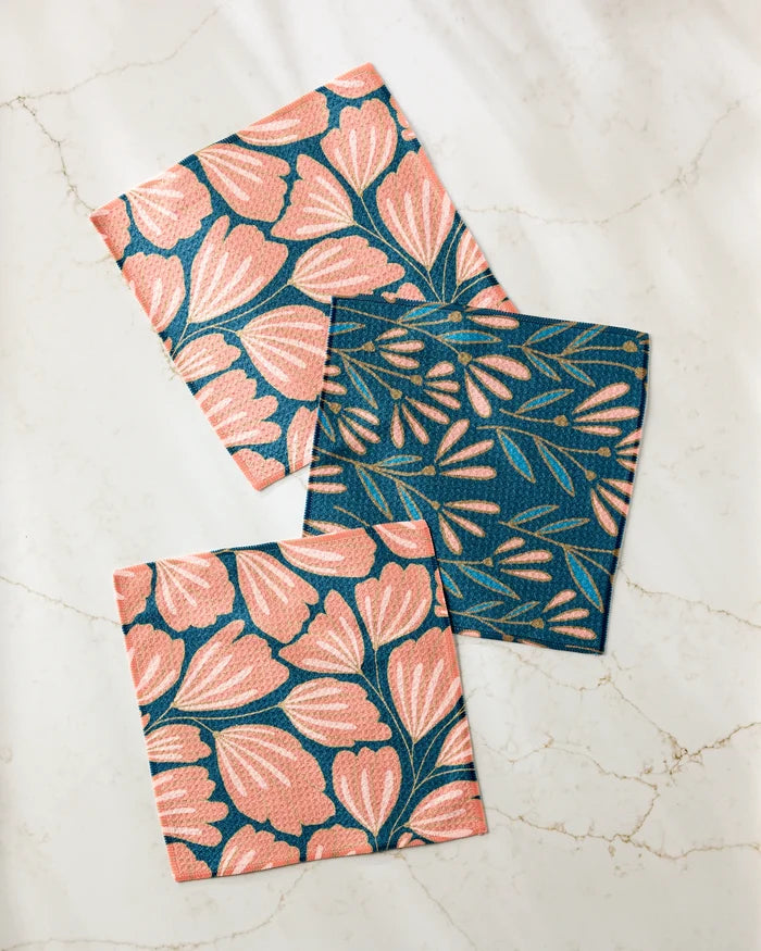Three eco-friendly Sheila Flower kitchen towels by Amy MacCready are displayed on marble: two with bold pink blooms on blue and one with delicate light pink leaves, a stylish addition to your reusable dishcloths set.