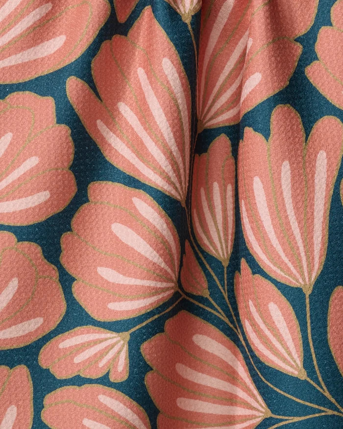 Close-up of Sheila recycled kitchen towel fabric by Amy MacCready, featuring large stylized pink flowers and green stems on a dark blue background with gentle folds creating subtle shadows and highlights.