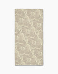 Shell Whisper by Geometry is a rectangular beige cloth napkin, made from post-consumer recycled materials, featuring a subtle, repeating light ginkgo leaf pattern and displayed flat on a white background.