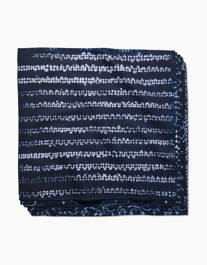 A neatly folded Shibo dinner napkin by GEOMETRY, made of dark blue Geosuede fabric with a white horizontal dotted tie-dye pattern, displayed on a white background.