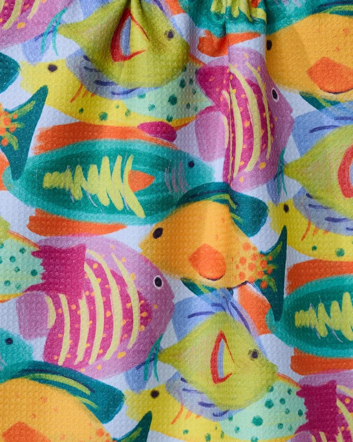 Geometrys Shoaling towel features a vibrant pattern of illustrated tropical fish in yellow, orange, green, pink, and purple overlapping on a white background. This colorful towel is quick-drying and perfect for summer days.