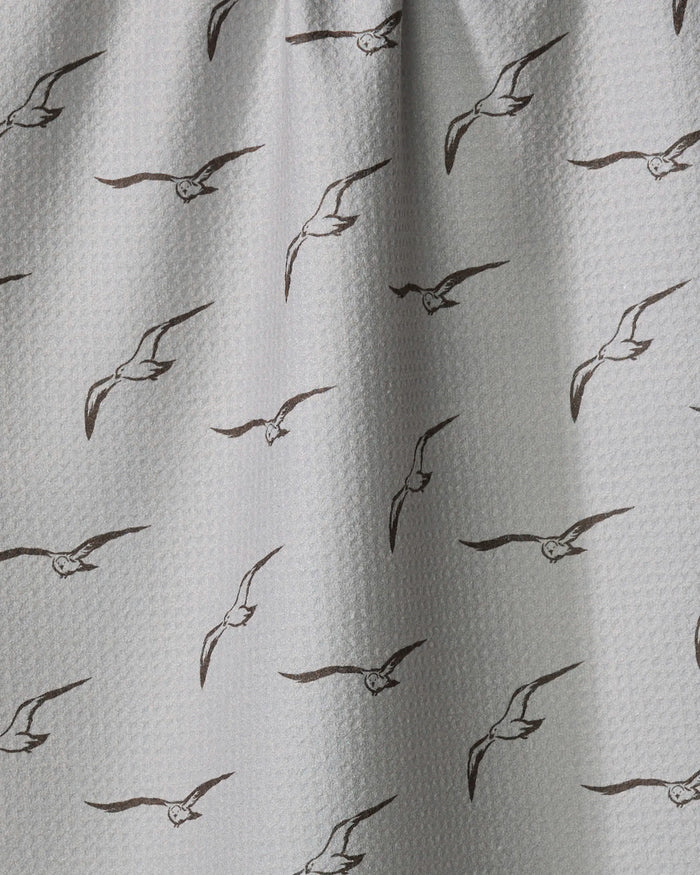 Shoreline Scout by Jenny Keller features white textured fabric with evenly spaced black line drawings of flying seagulls. Slightly gathered at the top, this charming tea towel adds a coastal touch to your kitchen.