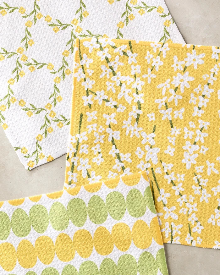 The Kayla Ann Signs of Springtime dishcloth set includes three super-absorbent towels—featuring green leaves and yellow flowers, white flowers on yellow, and green and yellow circles—all crafted from recycled materials.