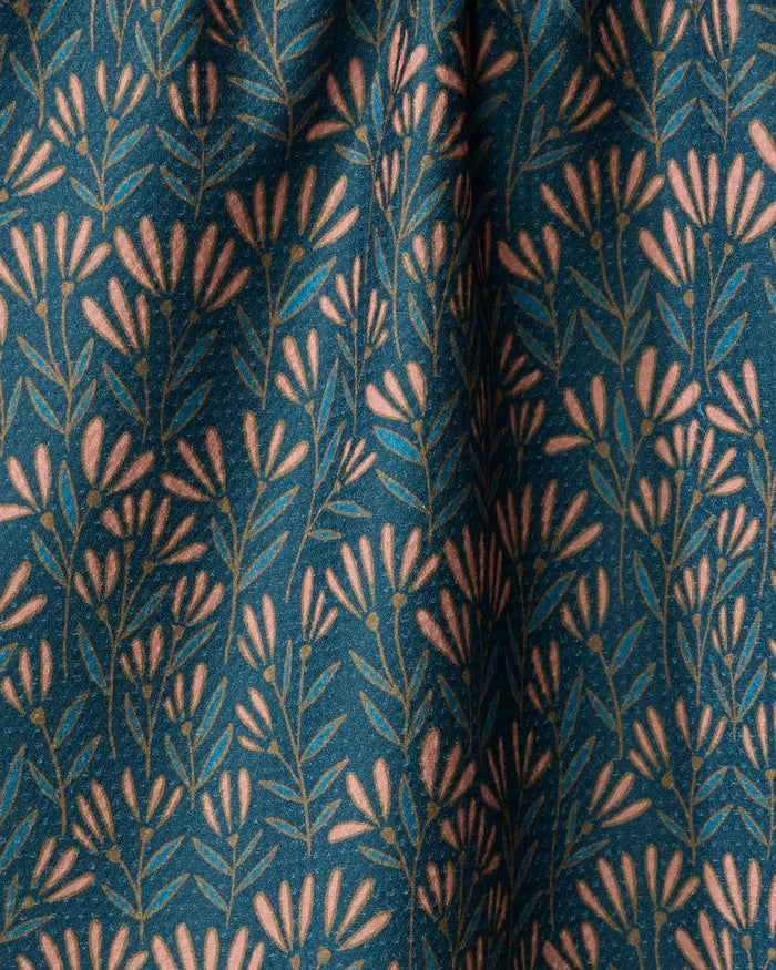 The Sirocco towel by Amy MacCready features dark teal fabric with pink, abstract floral stems and leaves. Its quick-drying material has a slightly bunched look, creating soft folds and subtle shadows for stylish functionality.