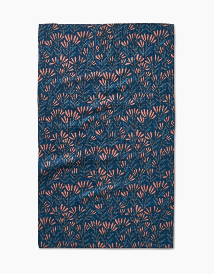 The Sirocco tea towel by Amy MacCready features dark blue Geoweave fabric with a dense pattern of small pink and light blue leafy branches. Ultra-absorbent, it is shown slightly wrinkled and laid flat on a white background.