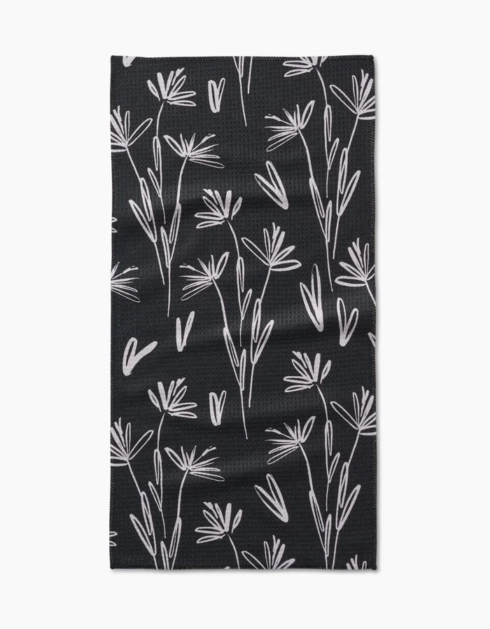 The Toboggan Avenue Sketchbook Dust bar towel is black, rectangular, and made from Geoweave fabric. It features a white minimalist botanical pattern with delicate, abstract flower and leaf outlines across the surface.