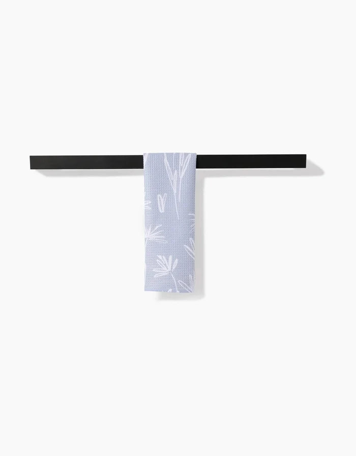 The Toboggan Avenue Sketchbook Floral bar towel, featuring a white botanical pattern on lavender Geoweave fabric, hangs neatly over a horizontal black towel bar against a plain white background.