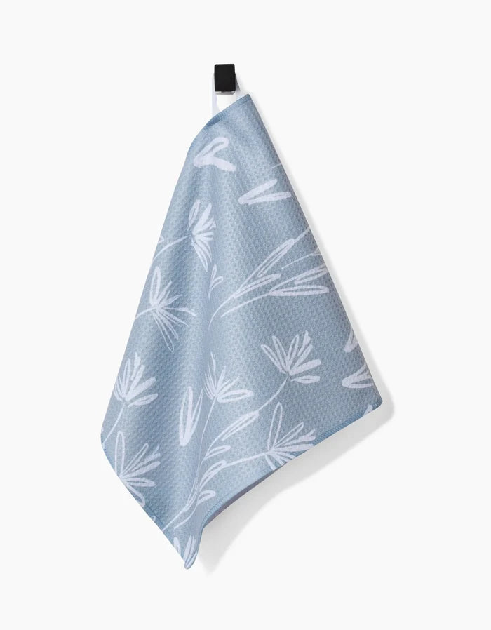 The Toboggan Avenue Sketchbook Floral Bar Towel, made from Geoweave fabric, features a light blue hue with a white abstract floral print and hangs by a black loop against a plain white background.