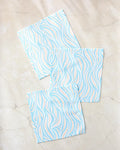 Three Rachel Parker Sky Willow Wave reusable cleaning cloths, featuring a blue and peach wavy pattern, are arranged in a loose triangle on a light marble surface.
