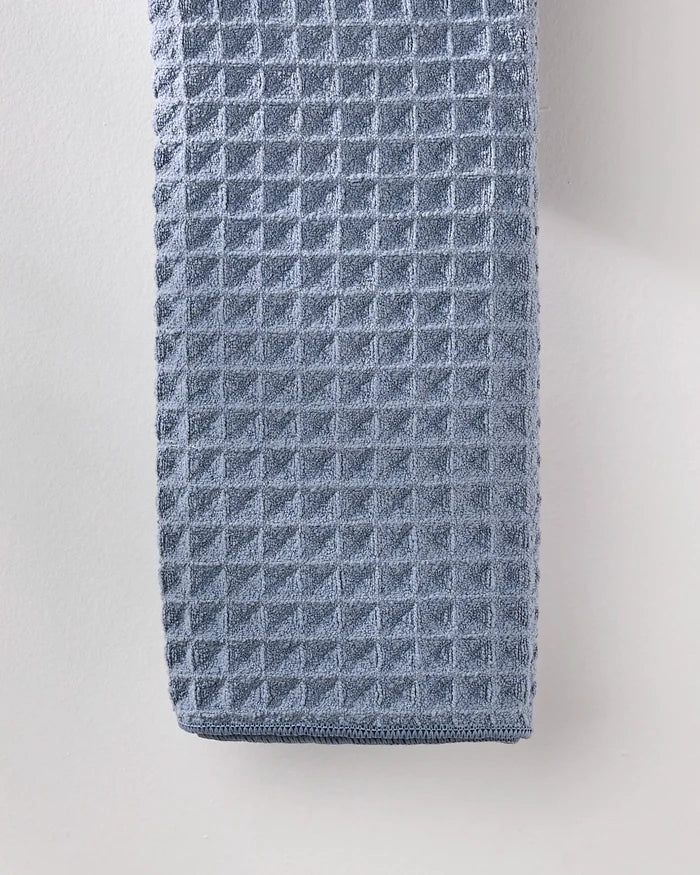 A close-up of the neatly folded GEOMETRY Sky waffle hand towel, featuring a textured finish, hanging against a light-colored wall.