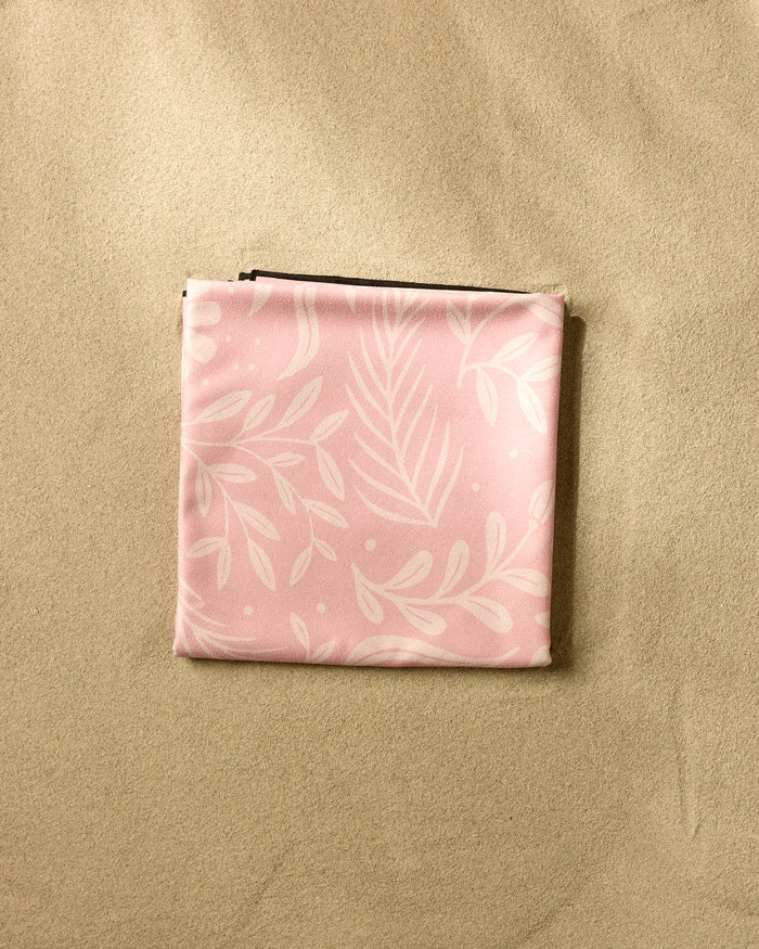 A folded piece of pink fabric with a white leaf pattern from the brand Small Steps, made using recycled materials, rests on a plain beige surface.