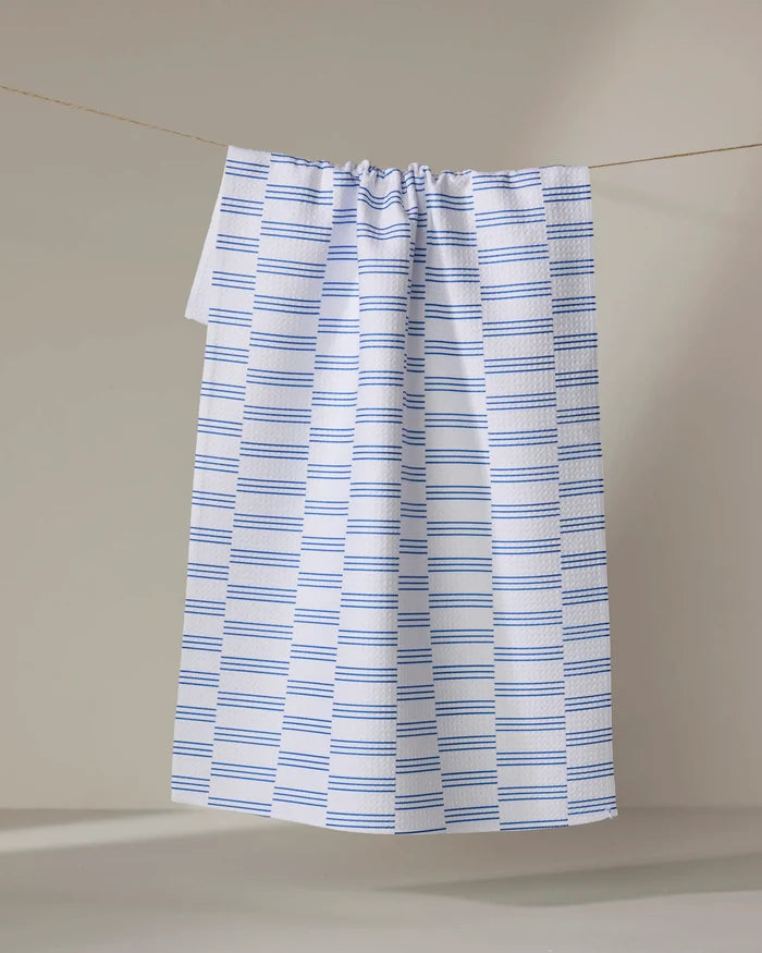 The Buy Guide’s Small Stripe - Navy tea towel, featuring absorbent white fabric with evenly spaced navy stripes, hangs from a string against a neutral background.