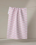 The Buy Guide's Small Stripe - Red tea towel, featuring evenly spaced horizontal red stripes on white, hangs from a string against a plain, neutral background.
