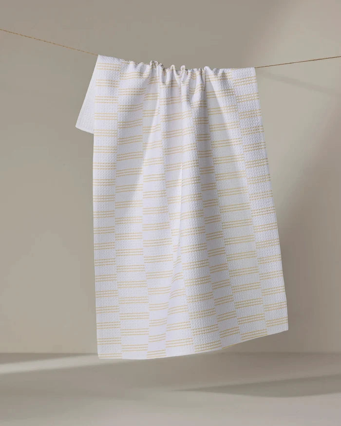 The Buy Guide's Small Stripe - Yellow kitchen tea towel, made from recycled materials, features a white base with a yellow grid pattern and hangs gathered at the top against a neutral background.