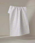 The Buy Guide's Small Stripe - Yellow kitchen tea towel, made from recycled materials, features a white base with a yellow grid pattern and hangs gathered at the top against a neutral background.