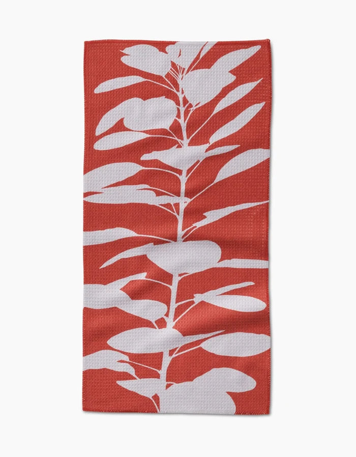 The PrintedPlant Smoketree bar towel showcases a bold red background with a white, stylized leafy plant silhouette extending vertically on its Geoweave fabric.