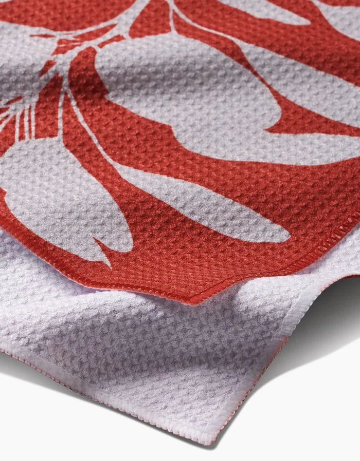A close-up of the PrintedPlant Smoketree Bar Towel, crafted from Geoweave fabric, shows its red and white botanical pattern, textured weave, and an upward-folded edge.