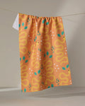 The Genna Blackburn "Snakes" tea towel in peach features a repeating yellow snake pattern with green leaves and white star-shaped flowers and is ultra-absorbent, perfect for hanging on your line.