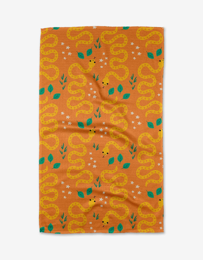 Add vibrant charm to your kitchen with Genna Blackburns Snakes tea towel, featuring yellow snakes, green leaves, and white stars on a solid orange background. Quick-drying and stylish—a must-have kitchen essential.