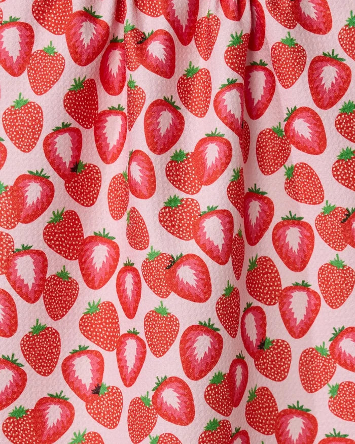 So Many Strawberries by Geometry features a close-up of pink fabric with a lively pattern of whole and sliced red strawberries and green leaves—fun, vibrant, and perfect for a tea towel.