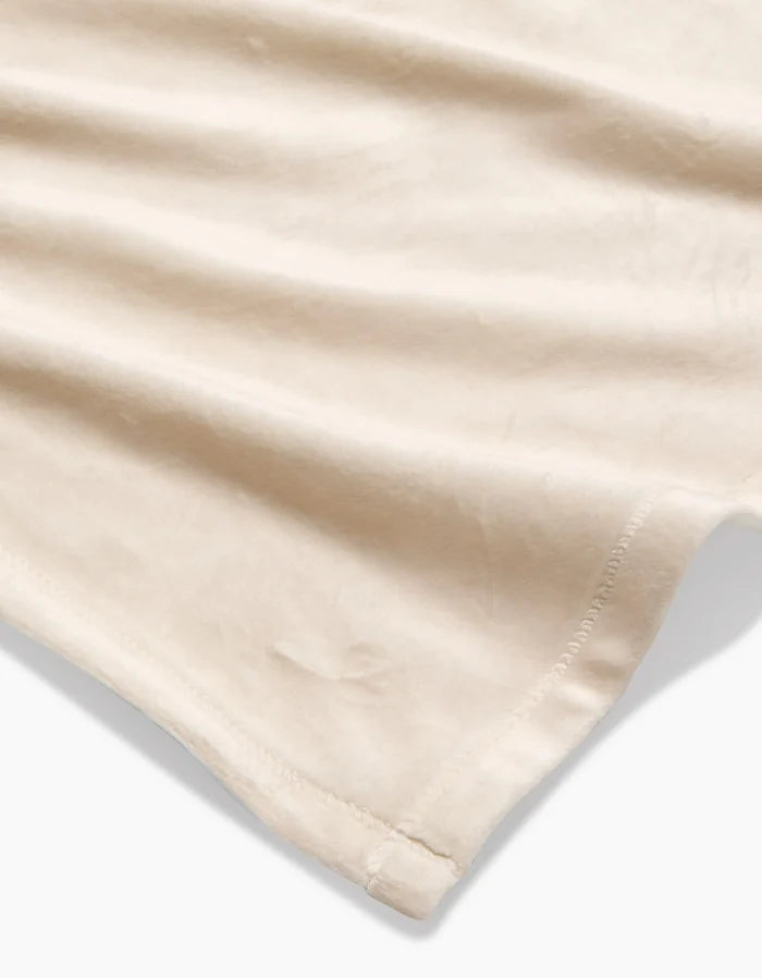 A close-up of GEOMETRY’s Soft Glow blanket, crafted from recycled materials in a soft beige shade, features a stitched hem and highlights its smooth texture and gentle folds.