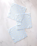 Three GEOMETRY "Soft Summer Sun" light blue textured recycled dishcloths with small yellow dots are arranged on a white marble surface.