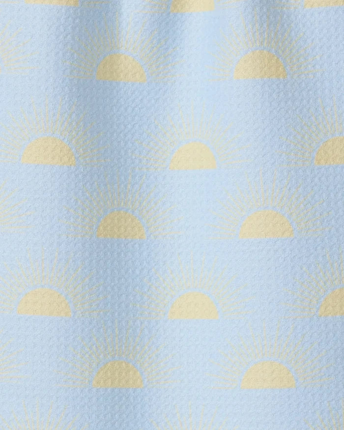 Soft Summer Sun by GEOMETRY is a light blue textured fabric made from recycled materials, featuring yellow half-sun sunrise motifs and radiating rays in an evenly spaced, repeating pattern.