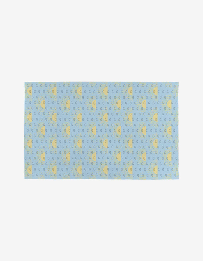 The GEOMETRY “Soft Summer Sun” is a rectangular blue cloth made from post-consumer recycled materials, featuring rows of yellow stars and crescent moons on a plain white background.