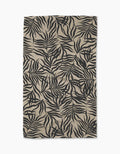 A rectangular beige Geometry Solar Flare tea towel from Geometry, featuring a bold black tropical leaf pattern on Geoweave fabric with slight wrinkles, photographed against a white background.