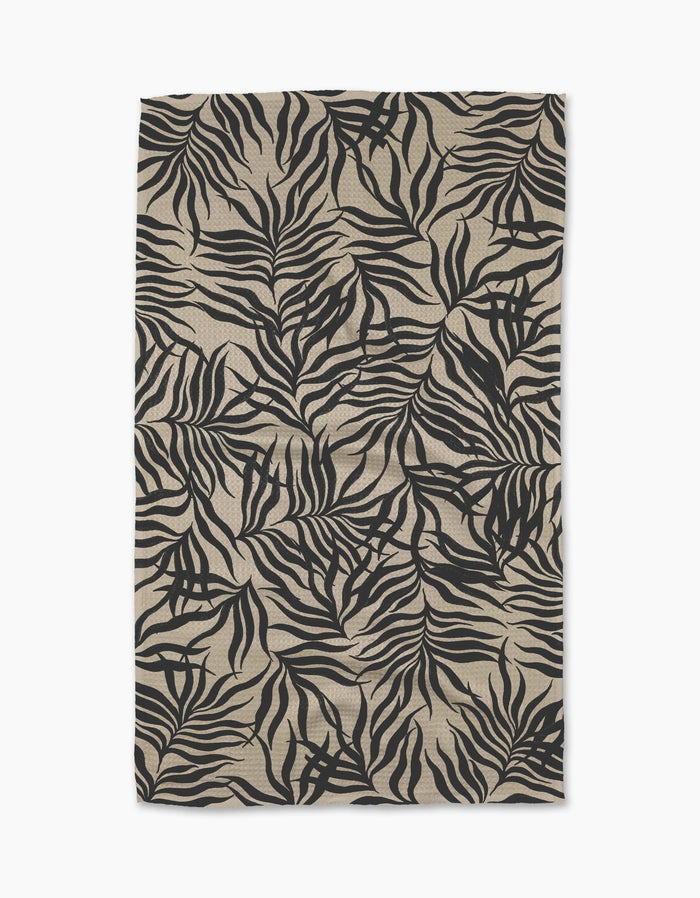A rectangular beige Geometry Solar Flare tea towel from Geometry, featuring a bold black tropical leaf pattern on Geoweave fabric with slight wrinkles, photographed against a white background.