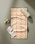 The Geometry Solar Power fitness towel is laid flat on a gray surface, with a white water bottle, cream dumbbells, and a folded white strap placed on and beside it. The towel features an eye-catching pattern and is made from recycled materials.