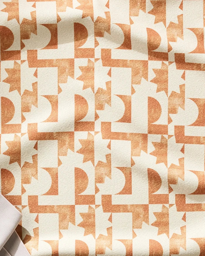 The Solar Power fitness towel by Geometry features a beige fabric with repeating light brown semi-circles, rectangles, and sunbursts. Retro-inspired and ultra-absorbent, it showcases subtle folds and shadows for a stylish workout look.