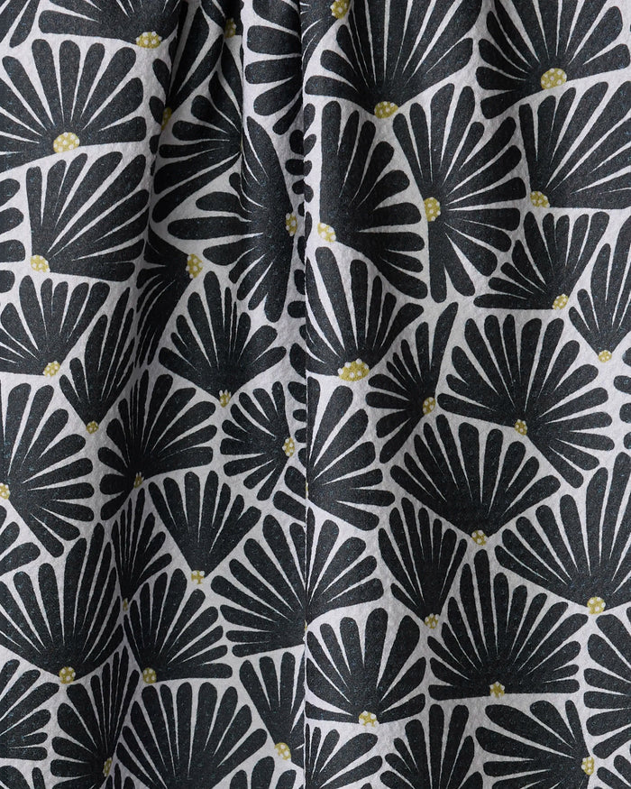 The Solie Black kitchen towel by Amy MacCready features a black fan-shaped leaf pattern with small yellow dots on light gray recycled fabric. Quick-drying with gentle folds and shadows, it adds depth and texture to your kitchen.