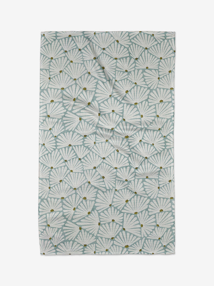 The Solie Teal Tea Towel by Amy MacCready features a repeating pattern of light blue and white fan-shaped leaves with small yellow accents, crafted from Geoweave fabric on a white background for a soft, airy look.