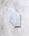Six eco-friendly "Something Blue" paper towels by GEOMETRY, featuring a subtle blue leaf pattern, are neatly stacked on a white marble surface.