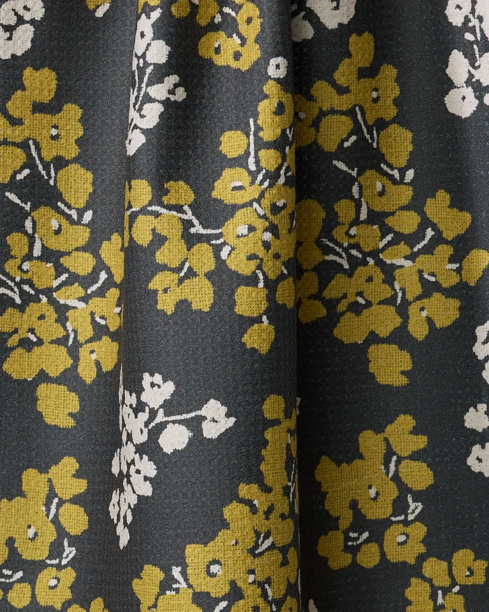 The Sonnet Ember tea towel by Geometry features yellow and white floral clusters and branches on dark fabric. Made from recycled materials, it’s ultra-absorbent with gentle folds and a subtly textured surface.