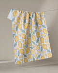 The Sour Lemon Stripes recycled kitchen towel by Hufton Studio features whole and sliced yellow lemons with green leaves, hanging from a line against a neutral background.