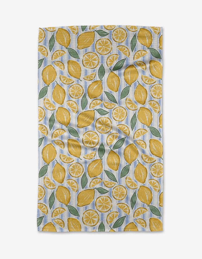 The Sour Lemon Stripes tea towel by Hufton Studio is an ultra-absorbent white kitchen towel featuring a repeating pattern of whole lemons, lemon slices, and green leaves scattered across its surface.