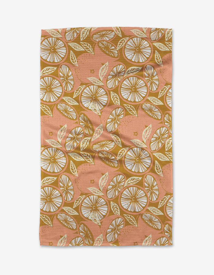 The Elisabeth Wing Spanish Grapefruit tea towel is eco-friendly in peach, adorned with a repeating citrus and leaf pattern in yellow, white, and brown tones, shown flat with gentle wrinkles.