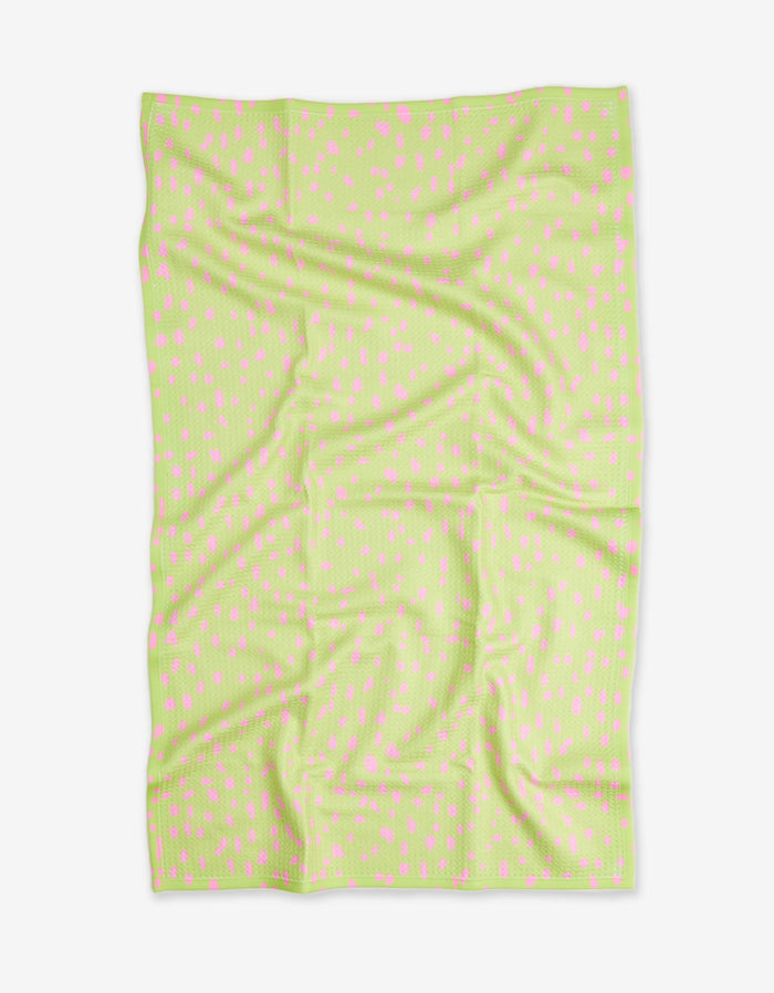 The Speckle Green blanket by GEOMETRY features a light green color with small, scattered pink dots. Made from recycled materials, it is shown flat with visible folds and creases on a white background.