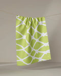 The Sissy Moon "Splash" kitchen towel in green, featuring a white abstract net-like pattern, hangs on a string against a neutral background.