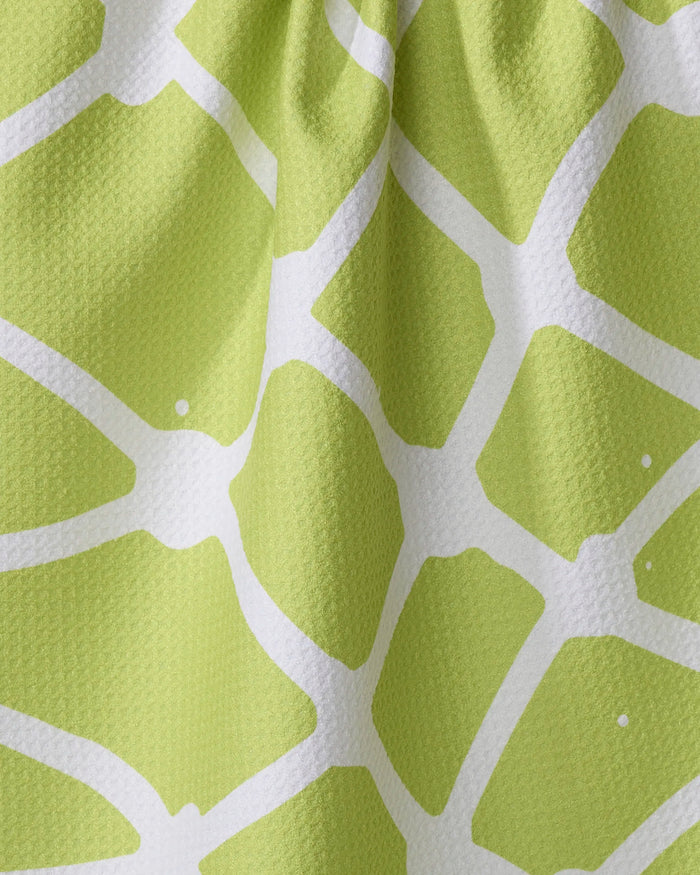 Close-up of Splash, a green kitchen towel by Sissy Moon, featuring a white geometric pattern reminiscent of leaves or turtle shells. Made from recycled materials, the textured fabric has a slightly wrinkled look.