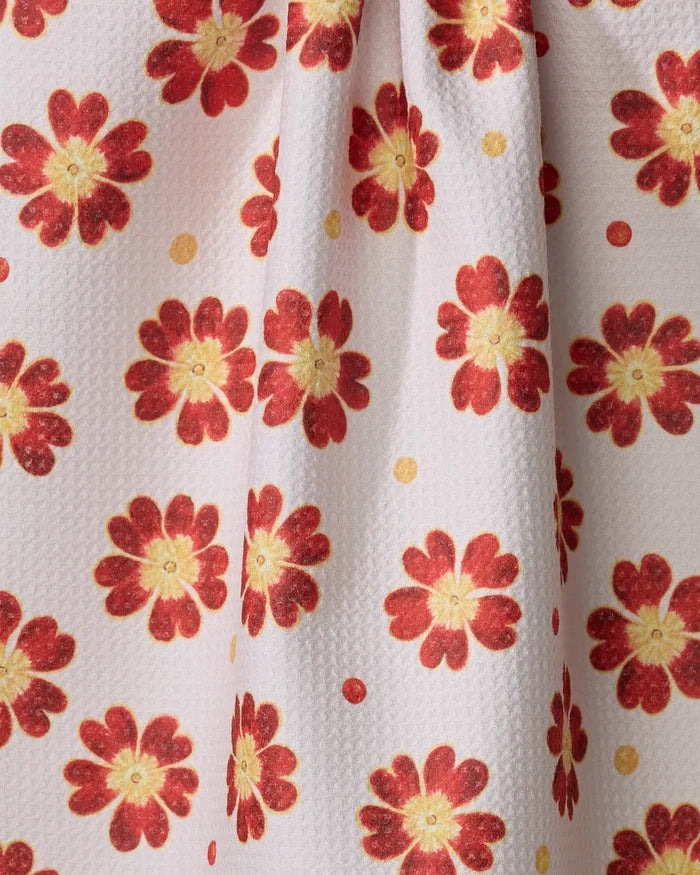 A close-up of the Linda Fox Spotty Floral kitchen tea towel, made from recycled materials, showing textured white fabric with red and yellow flowers, yellow dots, and a central pleat for soft folds.