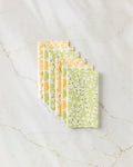 Six Kayla Ann "Spring Bounty" reusable paper towels with yellow and green floral patterns are neatly arranged in a row on a white marble surface with light brown veining.