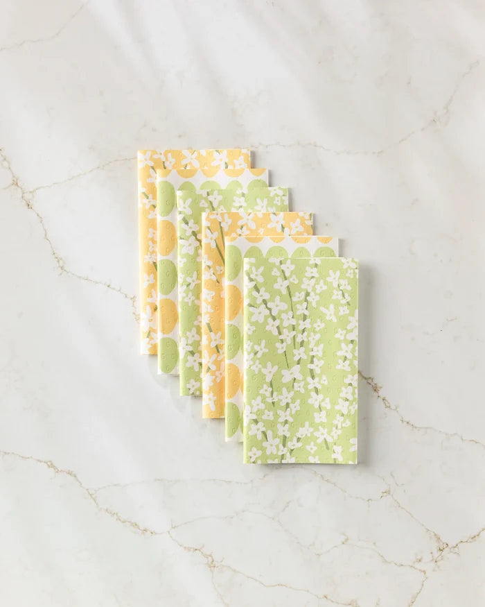 Six Kayla Ann "Spring Bounty" reusable paper towels with yellow and green floral patterns are neatly arranged in a row on a white marble surface with light brown veining.